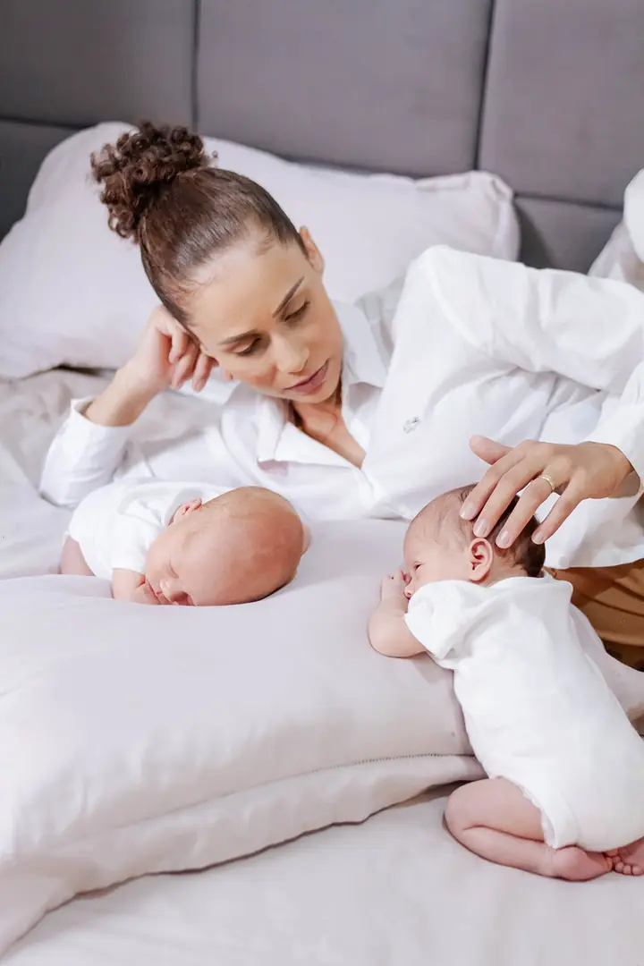 Bebês gêmeos dormindo tranquilos na cama enquanto Laís os observa